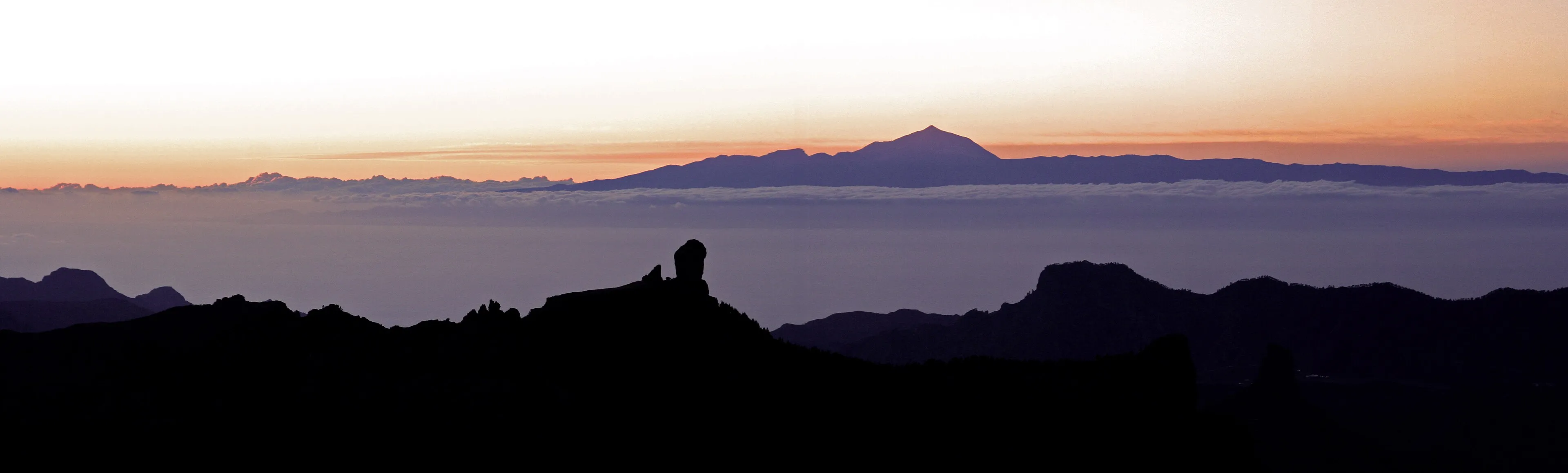 Roque Nublo in silhouette above a sea of clouds, with Teide on Tenerife on the horizon at sunset